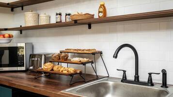 A kitchen with a stainless steel sink, a toaster, a microwave, and shelves with jars and bread.