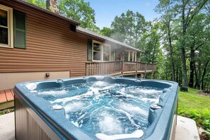 Ein Whirlpool vor einem Holzhaus mit einem Balkon mit Blick auf eine bewaldete Landschaft.