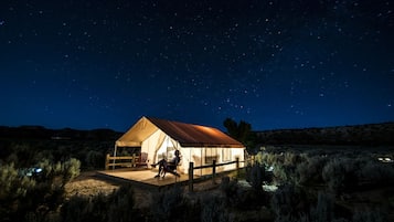 A tented accommodation with a wooden deck and a person seated inside.