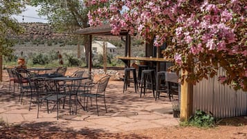 An outdoor patio with tables and chairs, a pergola with pink flowers, and a building in the background.