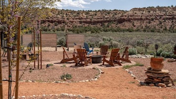 An outdoor seating area with wooden chairs and a table, surrounded by a garden with rocks and sparse vegetation.