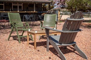 Une table en bois, accompagnée de deux chaises, l’une verte et l’autre marron, placée dans un espace extérieur dont le sol est recouvert de gravier.