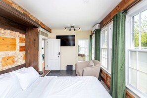 Ein Hotelzimmer mit einem Bett, einem Sessel, einem Fernseher und einem fenster mit Vorhängen.