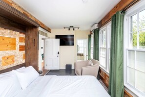 Ein Hotelzimmer mit einem Bett, einem Sessel, einem Fernseher und einem fenster mit Vorhängen.
