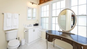 Een badkamer met toilet, wastafel, badkamermeubel en grote ramen.