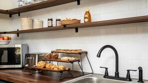 Een keuken met een roestvrijstalen spoelbak, een broodrooster, een magnetron en planken met potten en brood.