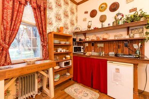 Une cuisine avec des étagères en bois, un four à micro-ondes, un réfrigérateur et une fenêtre avec des rideaux.