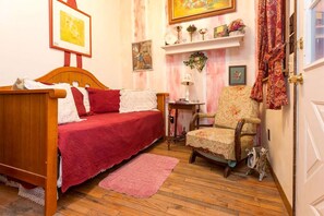 Un dormitorio con cama de madera, una silla, una mesita y una estantería con adornos.