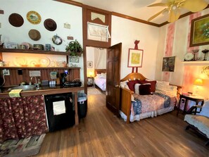 A compact room with a kitchenette, a bed, a desk, and a ceiling fan.