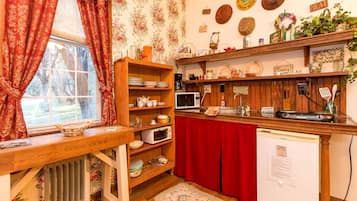 Una cocina con estantes de madera, microondas, refrigerador y una ventana con cortinas.
