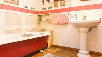 Ein Badezimmer mit einer roten Badewanne, einem weißen Waschbecken auf Säule und einem Spiegel darüber.