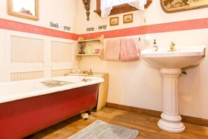 A bathroom with a red bathtub, a white pedestal sink, and a mirror above the sink.