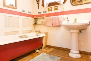 Un baño con una bañera roja, un lavamanos blanco y un espejo sobre el lavamanos.