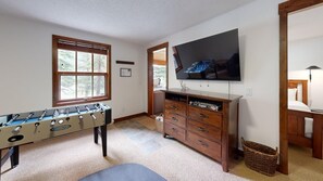 Ein Zimmer mit Tischfußballtisch, Wandfernseher und einer Holzkabine mit Schubladen.