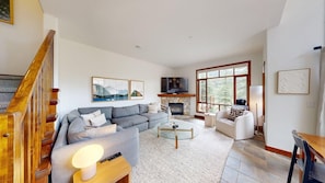 A modern living room with a sofa, coffee table, fireplace, TV, and a staircase.