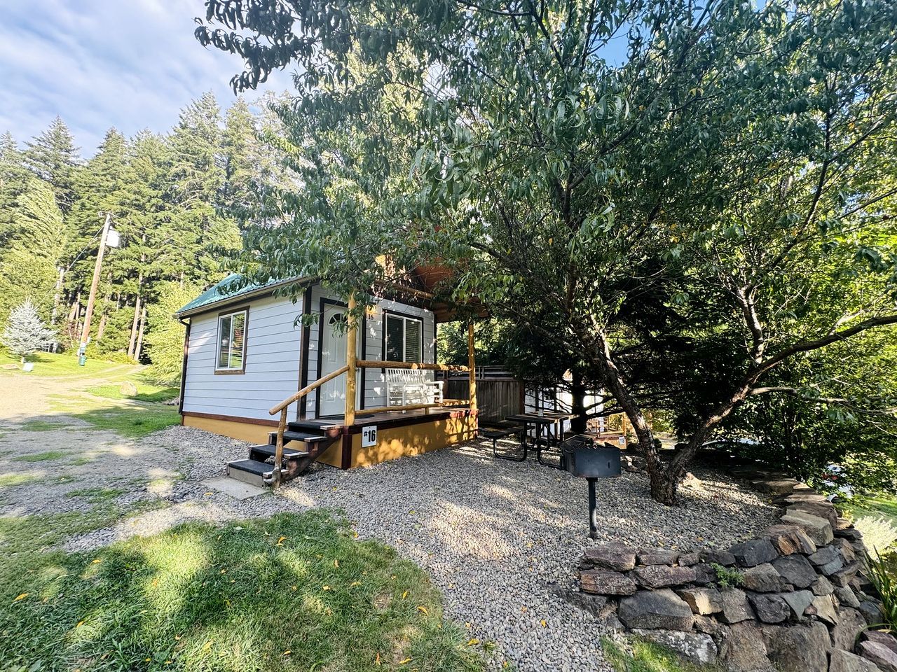 A small cabin with a porch, a gravel driveway, and a stone wall.