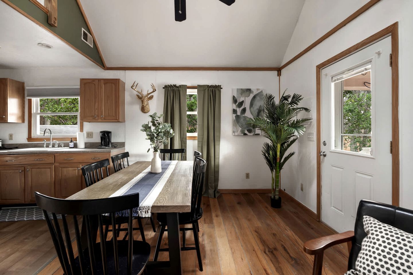 A dining area with a wooden table, chairs, a vase with greenery, and a large potted plant.