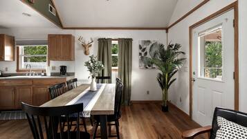A dining area with a wooden table, chairs, a vase with greenery, and a large potted plant.