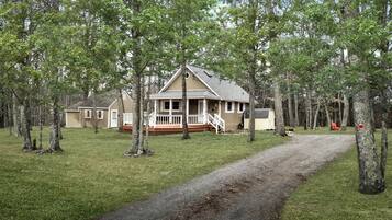 A house with a porch, surrounded by trees, and a gravel path leading to it.