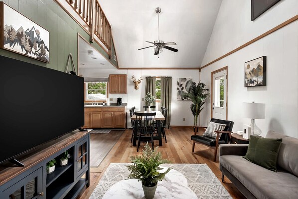 A spacious living room with a television, a dining area, and a kitchen in the background.