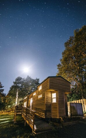 A wooden cabin with a porch, a small deck, and a fenced yard.