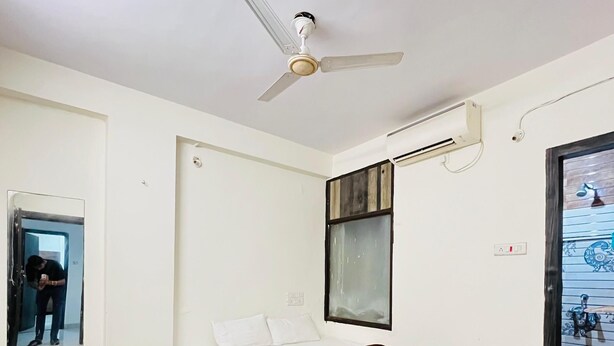 Une chambre à coucher comprenant un lit, un ventilateur de plafond, une fenêtre et un appareil de climatisation.