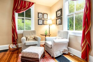 Una habitación acogedora con dos sillones a rayas, una mesita con una lámpara y cuadros enmarcados en la pared.