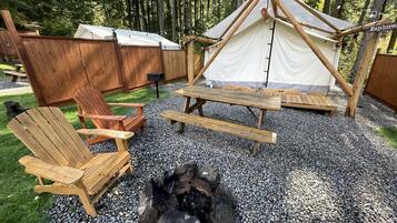 En campingplads med et telt, bålsted og træmøbler.