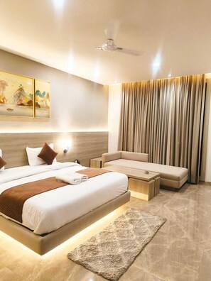 A modern hotel room with a large bed, a sofa, a coffee table, and a ceiling fan. - THE RIVERSIDE INN (Vidisha)
