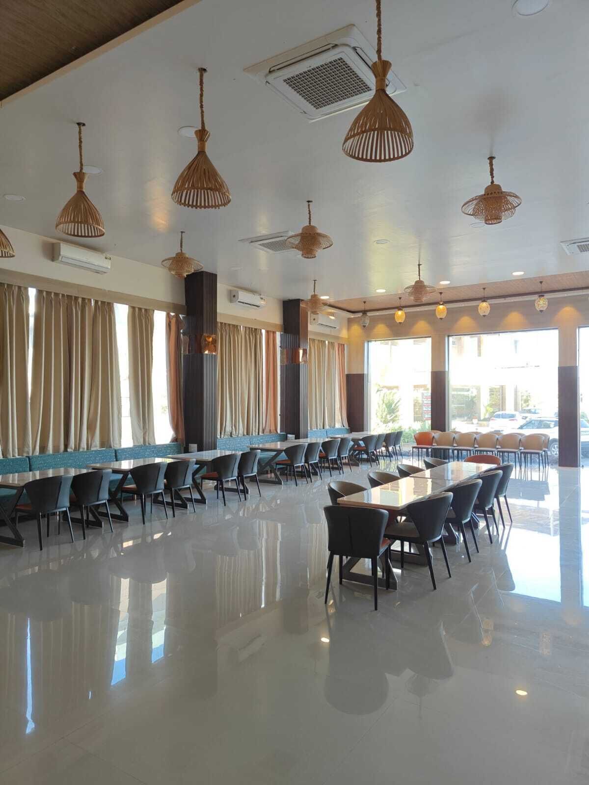 Un comedor espacioso con mesas y sillas largas, ventiladores de techo y ventanas amplias que permiten la entrada de luz natural.
