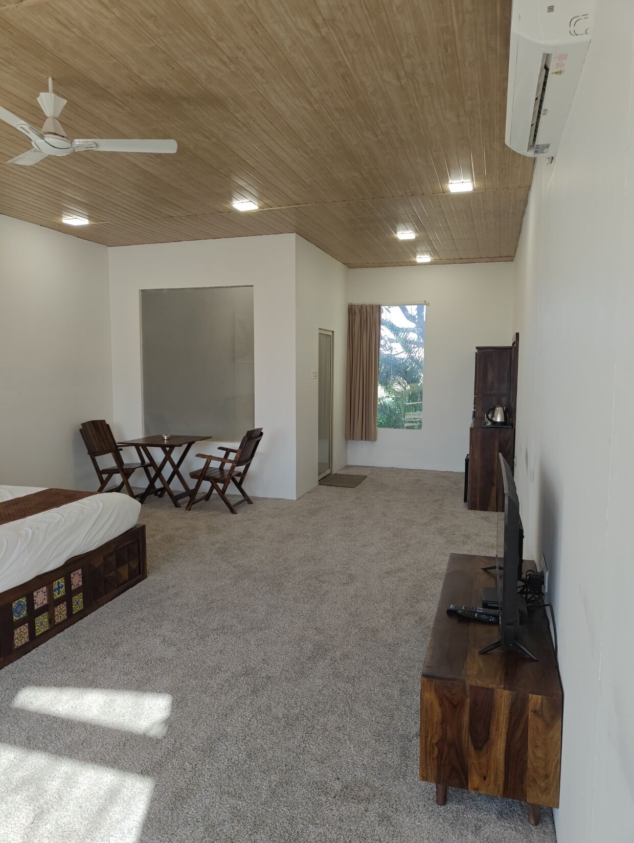 A bedroom with a bed, a desk, a chair, a television, and a ceiling fan.