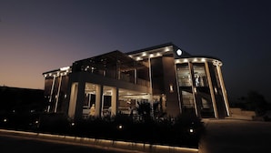 A modern hotel with a curved facade, large windows, and a covered entrance area. - THE RIVERSIDE INN (Vidisha)