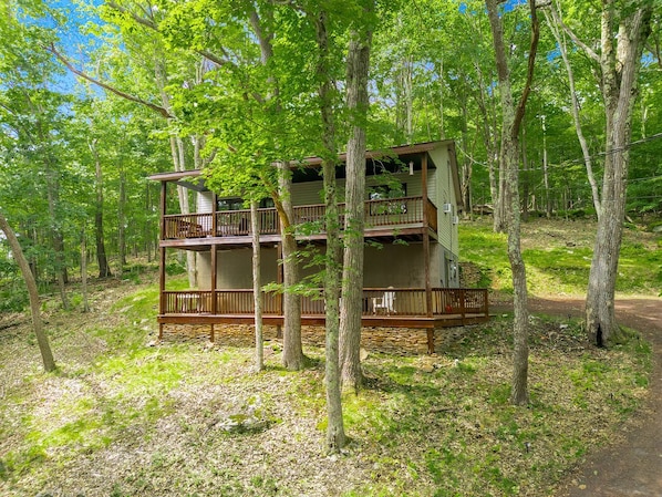 A two-story cabin with a balcony, surrounded by trees.