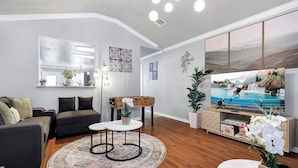 A modern living room with a sofa, coffee table, TV, and decorative plants. - Hot Tub Haven Yard Swing Set BBQ Games Desk WiFi (San Antonio)