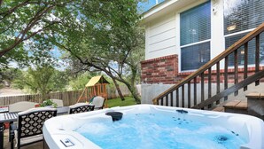 A hot tub in a backyard with a wooden deck, a patio table, and chairs. - Hot Tub Haven Yard Swing Set BBQ Games Desk WiFi (San Antonio)