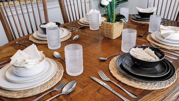 A dining table set with plates, bowls, cutlery, and glassware, surrounded by chairs. - Hot Tub Haven Yard Swing Set BBQ Games Desk WiFi (San Antonio)