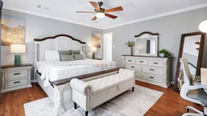 A bedroom with a bed, nightstands, a bench, a desk, a chair, a ceiling fan, and a mirror. - Hot Tub Haven Yard Swing Set BBQ Games Desk WiFi (San Antonio)