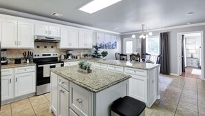 A modern kitchen with white cabinetry, granite countertops, a central island, and a large window providing natural light. - Hot Tub Haven Yard Swing Set BBQ Games Desk WiFi (San Antonio)
