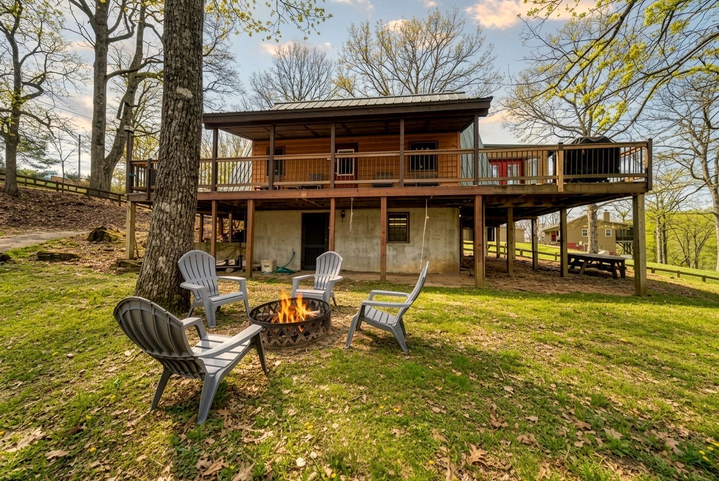 Eine zweistöckige Holzhütte mit einer Terrasse, Sitzgelegenheiten im Freien und einer Feuerstelle.