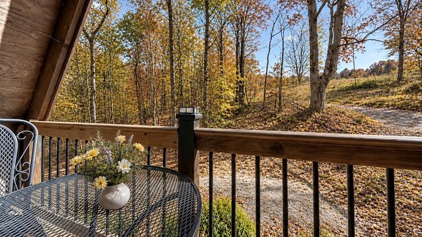 Eine Holzterrasse mit einem Metalltisch und -stühlen, mit Blick auf ein bewaldetes Gebiet im Herbstlaub.