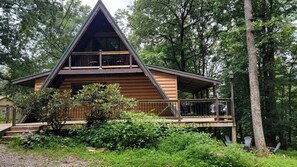 A cabin with a triangular roof, a balcony, and surrounded by greenery.