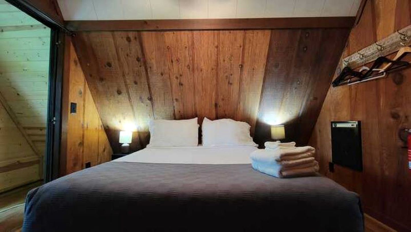 A bedroom with a wooden ceiling, a bed with white linens, two bedside lamps, and a stack of folded towels.
