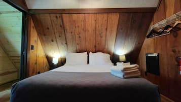 Een slaapkamer met een houten plafond, een bed met witte lakens, twee bedlampjes en een stap opgevouwen handdoeken.