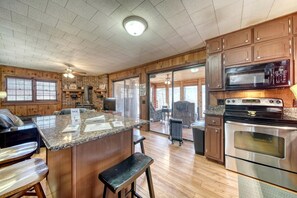 A kitchen with granite countertops, stainless steel appliances, wooden cabinets, and a large island with bar stools. - Cozy Getaways in this Cute A-Frame Cabin in Suches, Georgia (Suches)