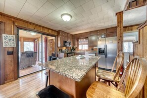 Une cuisine dotée de meubles en bois, d’un plan de travail en granit, d’appareils électroménagers en acier inoxydable et d’un coin repas avec des chaises en bois.