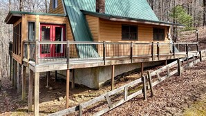 Eine Hütte mit grüner Dachdeckung, einer roten Tür und einer Holzterrasse.
