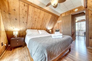 A wooden-paneled bedroom with a bed, bedside lamps, and a view of the outdoors.