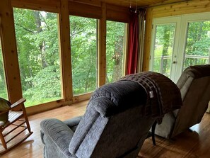 Une pièce dotée de grandes fenêtres, d’une chaise, d’un fauteuil à bascule et d’un plancher en bois.
