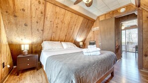 Ein Schlafzimmer mit Holzwandpaneelen, einem Bett, Nachttischlampen und Blick ins Freie.