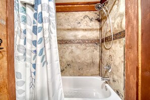 A bathroom with a shower, a bathtub, and a curtain with a leaf pattern. - Cozy Getaways in this Cute A-Frame Cabin in Suches, Georgia (Suches)